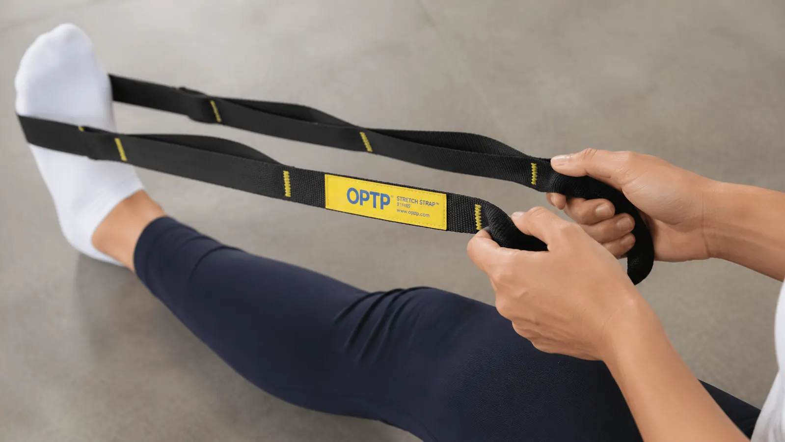 Close-up of hands gripping multiple loops on a yellow nylon stretch strap during a seated hamstring stretch