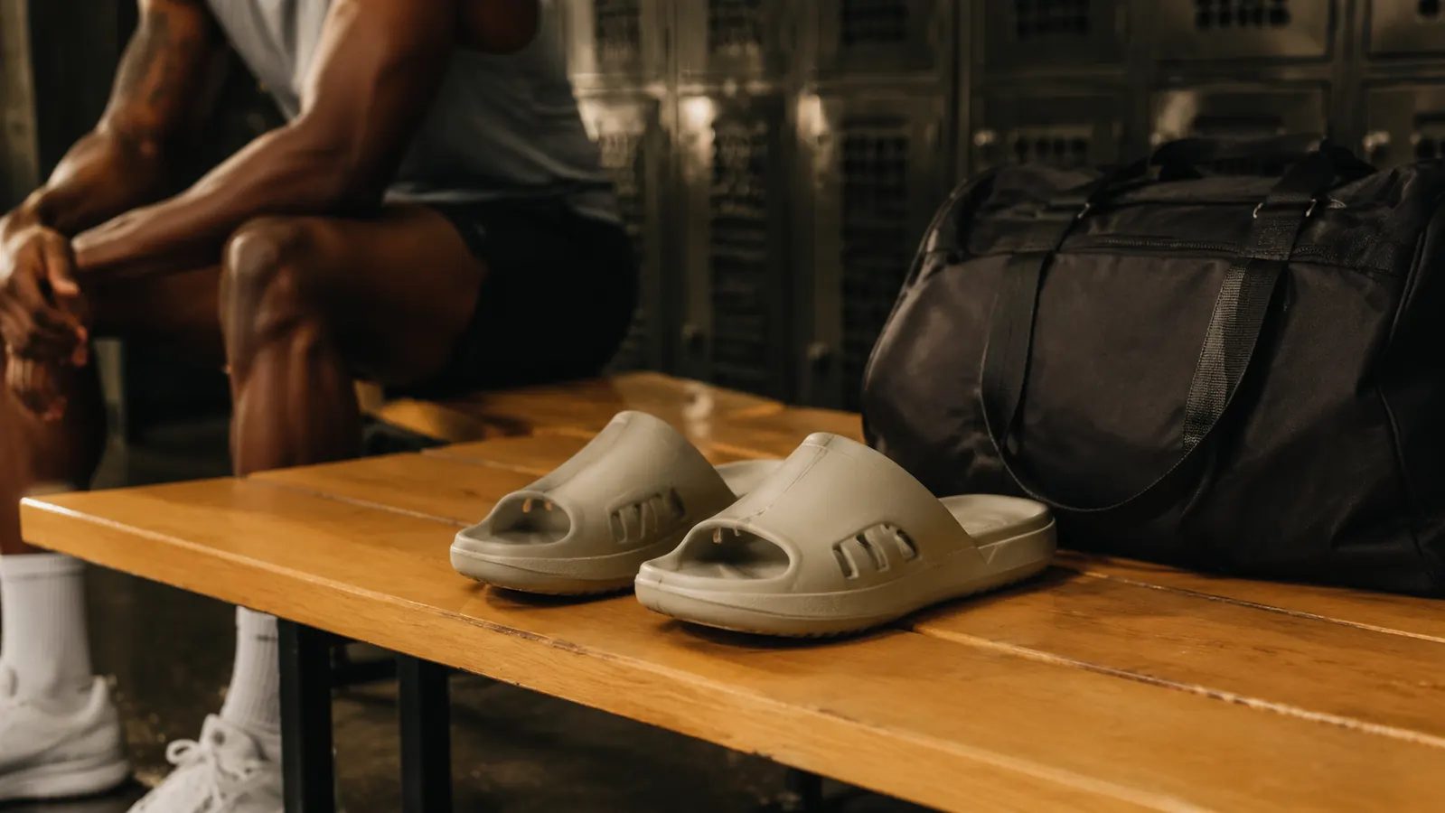 Two recovery slides side by side on a gym bag next to a water bottle and running shoes